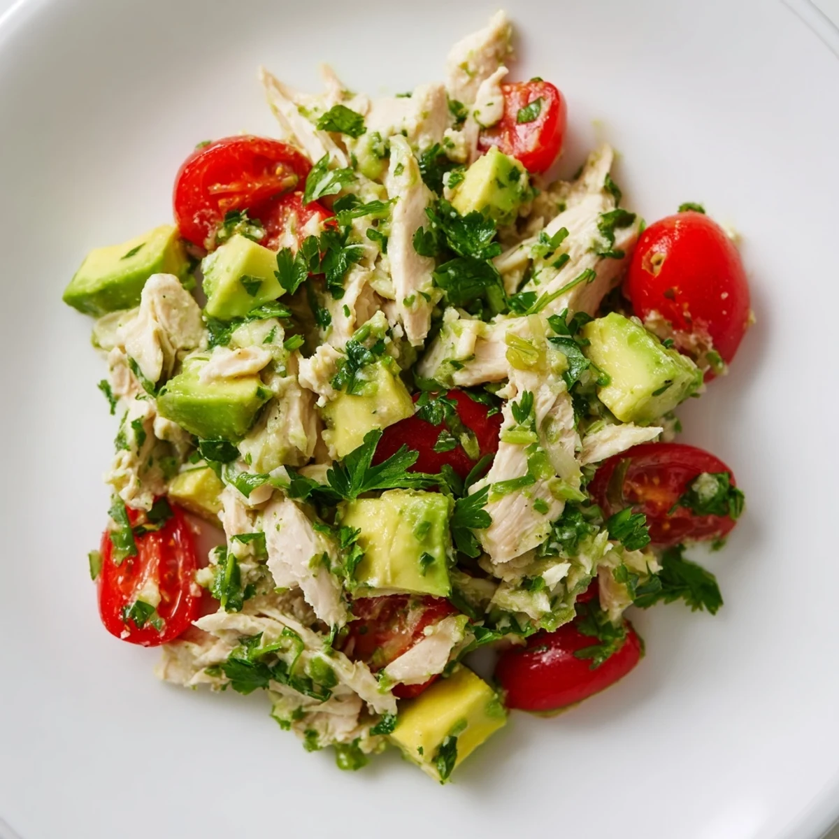 Frisch zubereitete Avocado Chicken Salad auf einer rustikalen Holzplatte mit Koriander, Limettenscheibe und Olivenöl.