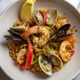 A close-up shot of steaming Spanish seafood paella, fragrant with saffron and herbs.