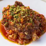 Close-up of golden-brown Osso Buco with rich tomato sauce and fresh gremolata garnish.