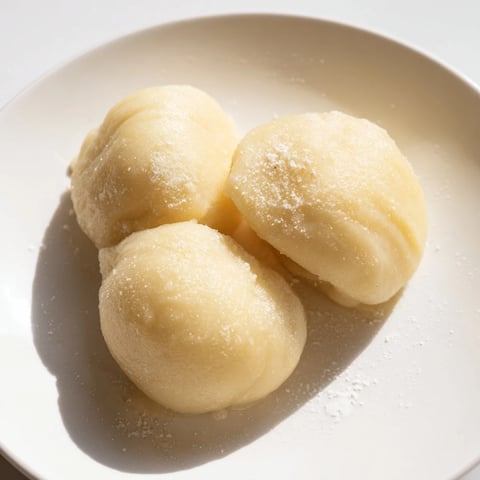 Fluffy, golden brown potato dumplings, ready to serve with savory gravy on a white plate.