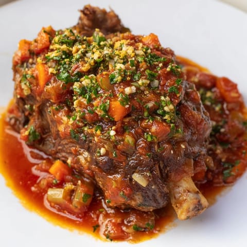 Close-up of golden-brown Osso Buco with rich tomato sauce and fresh gremolata garnish.