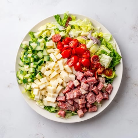 Ein großer Salat mit gehacktem Hühnchen, Salami, Provolone und frischem Salat, belegt mit Tomaten und Roten Zwiebeln, serviert mit einem tangigen Kräuterdressing auf einer rustikalen Holzplatte.