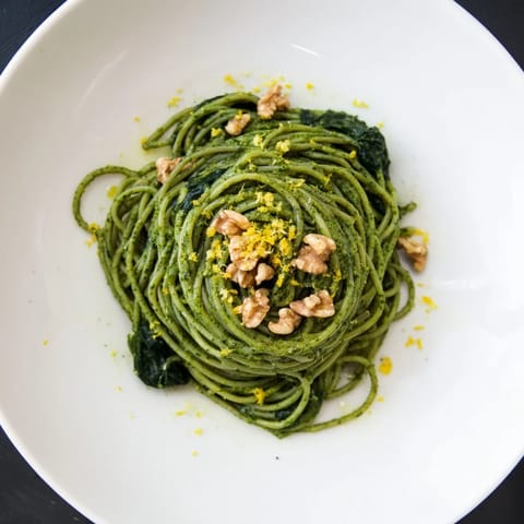 A vibrant bowl of Creamy Spinach Walnut Pasta, garnished with lemon zest and freshly ground black pepper.