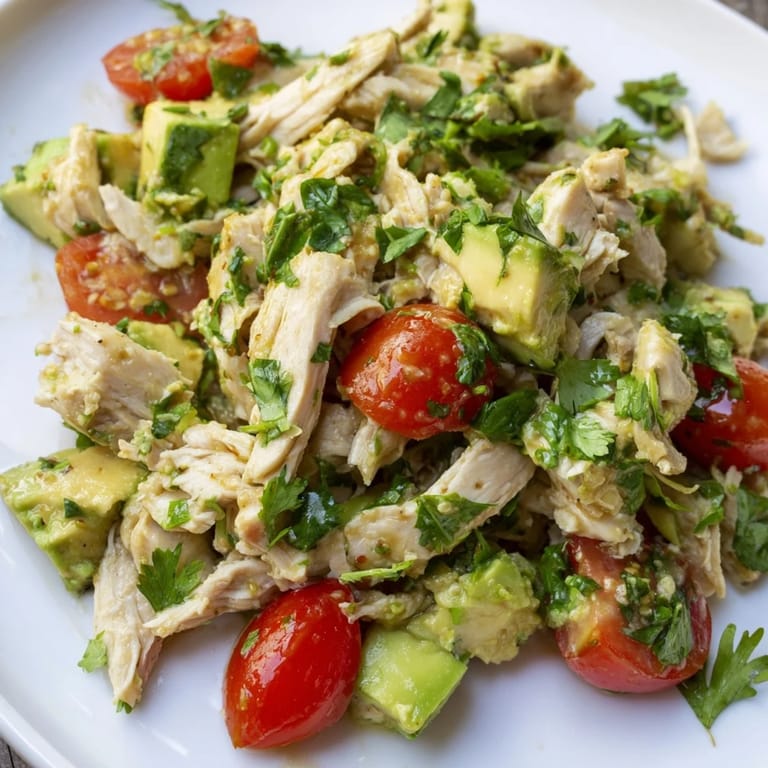 Eine cremige Avocado Chicken Salad mit glasigen Tomaten, roten Zwiebeln und grünen Gurkenwürfeln, fertig zum Servieren.